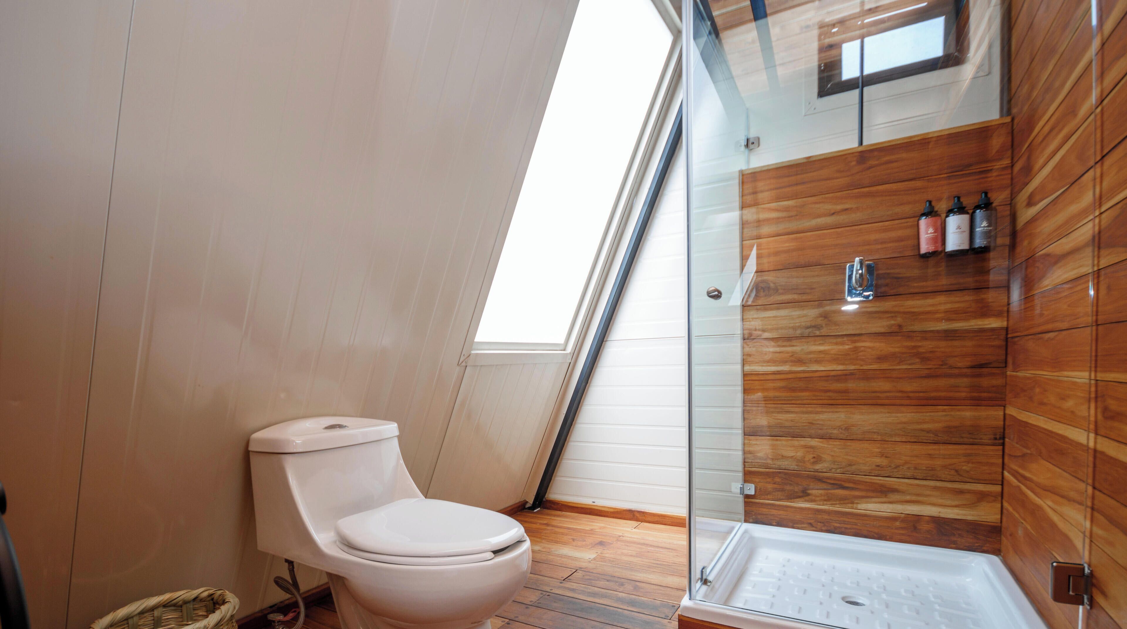 Un baño moderno con ducha envuelta en vidrio, inodoro blanco y paneles de madera en las paredes.
