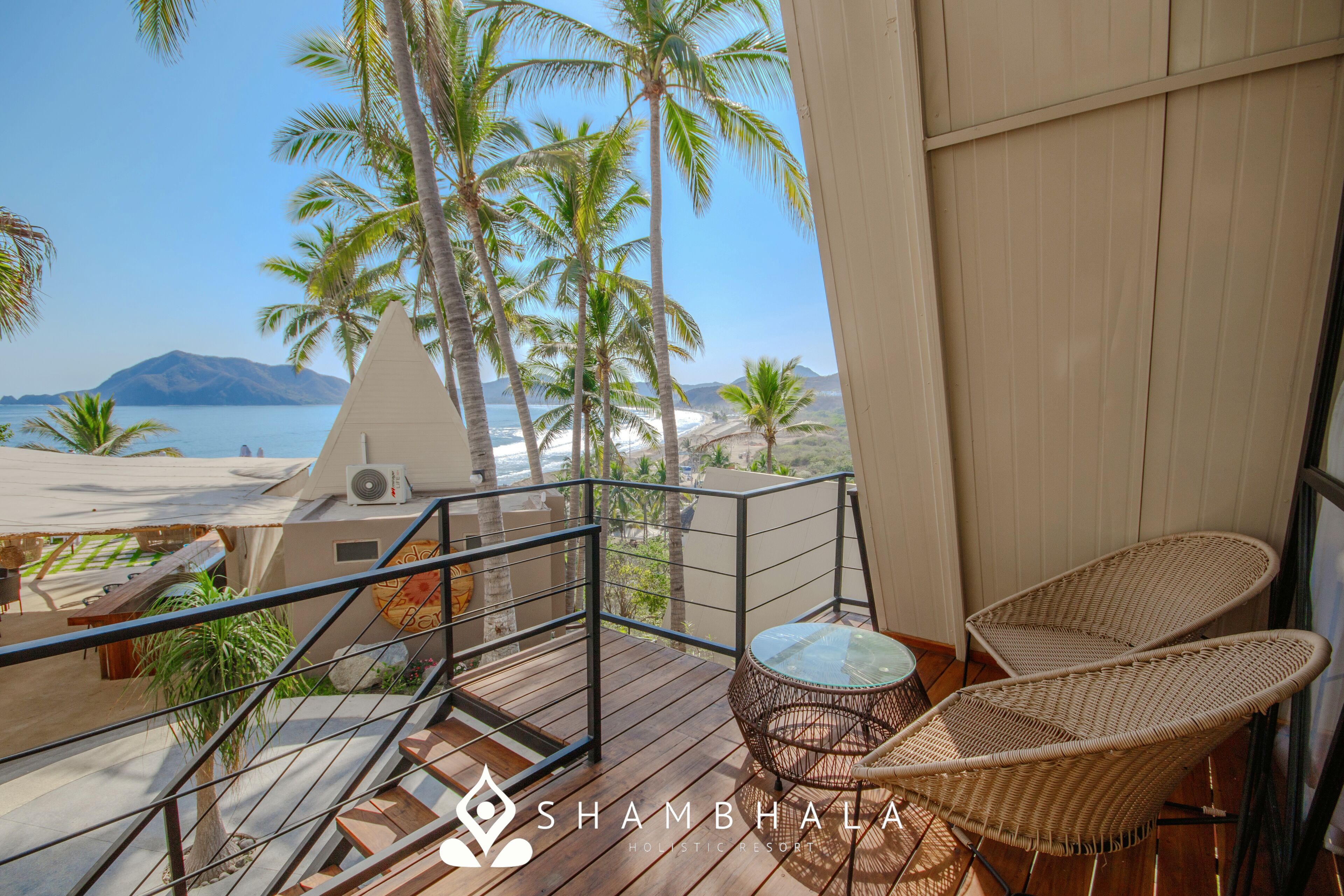 Ein Balkon mit Korbstühlen, einem kleinen Tisch und Blick auf Strand und Meer.