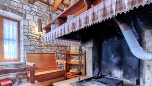 A rustic stone wall, wooden furniture, a fireplace with a chimney, and a window with curtains. - Villa Christina by Interhome (Tinjan)