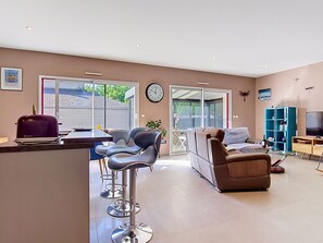 Ein modernes Wohnzimmer mit einer Couch, Sesseln, einem Couchtisch, einem Fernseher und einem Bücherregal.