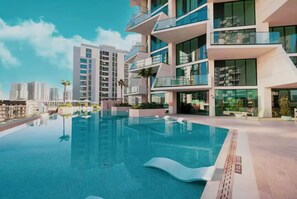 Ein modernes Gebäude mit Pool auf dem Dach, umgeben von hohen Wohnhäusern.