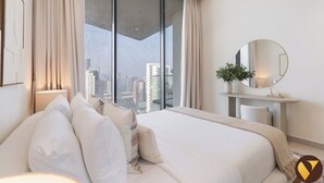 Un hotel moderno con una cama grande, una mesita de noche con espejo, una planta en maceta y vistas de la ciudad a través de ventanas de pared a techo.