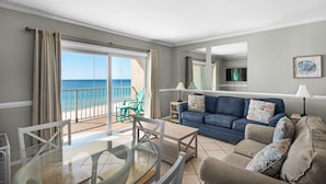 Een kamer met balkon en uitzicht op zee, een blauwe bank en een glazen eettafel.