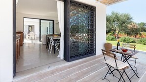Une terrasse moderne avec une table et des chaises, une vue sur le jardin et une porte-fenêtre coulissante donnant sur un espace int érieur.