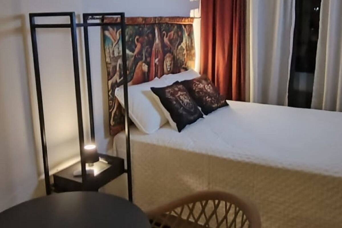 A hotel room with a bed, a small table, a chair, and a painting on the wall.