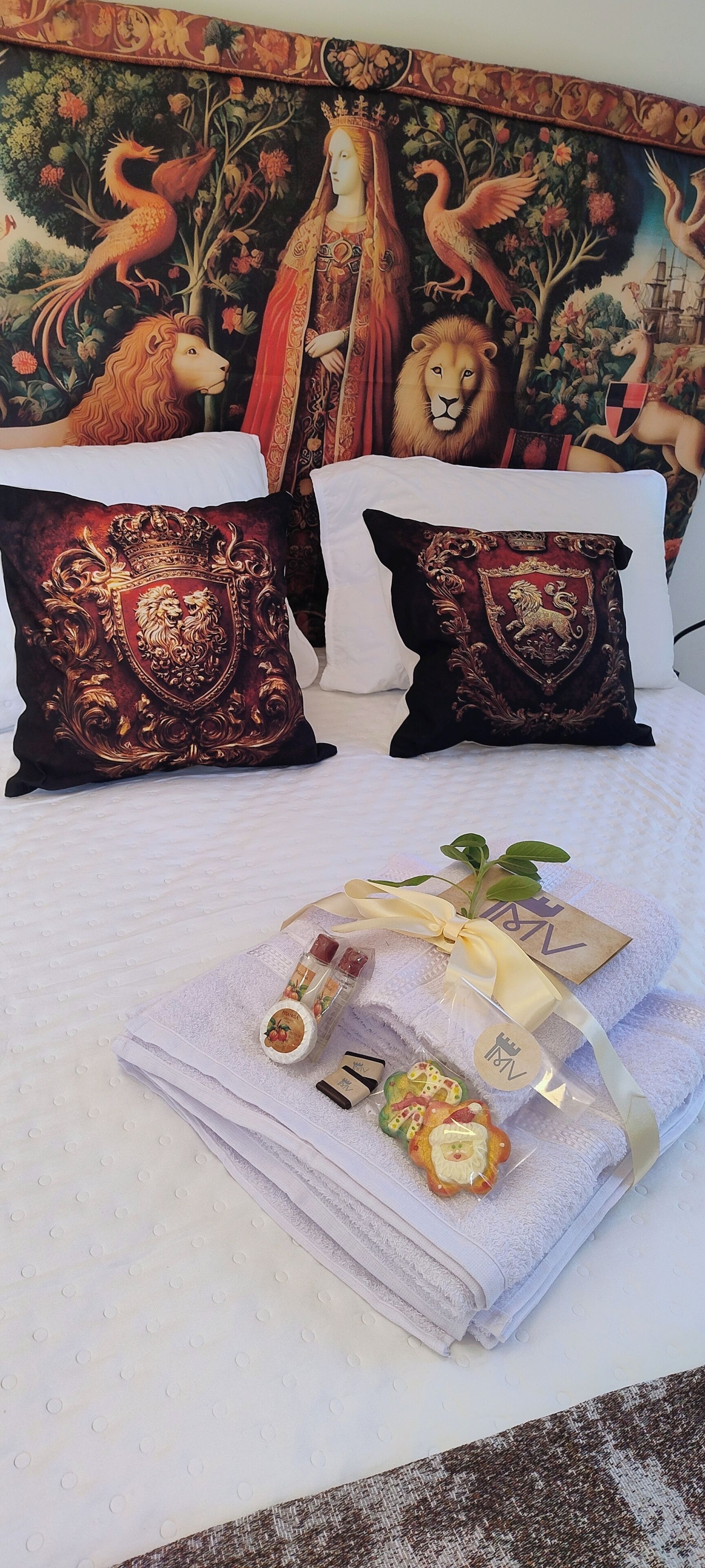 A bed with decorative pillows, a towel with a ribbon, and a tapestry with a lion and peacock.
