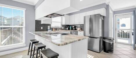 A modern kitchen with a large island, bar stools, stainless steel appliances, and a view to the outside.
