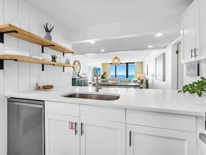Une cuisine moderne avec des meubles blancs, un évier en acier inoxydable et une vue sur la salle à manger.