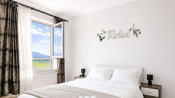 Een slaapkamer met een bed, twee nachtkastjes, een raam met gordijnen en een muurstickers.