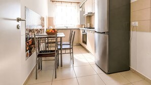 Een moderne keuken met een roestvrijstalen koelkast, een eettafel met stoelen en een raam met gordijnen.