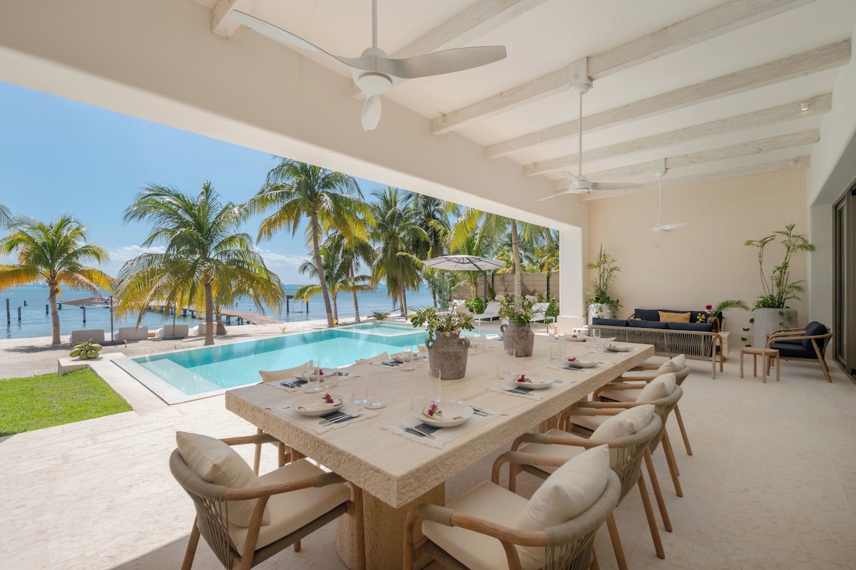 A poolside dining area with a view of the ocean, a ceiling fan, and outdoor seating.