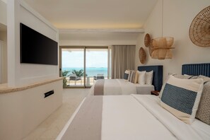 A hotel room with a large TV, two beds, a balcony with a view, and decorative wall hangings. - La Coleccion (Isla Mujeres)
