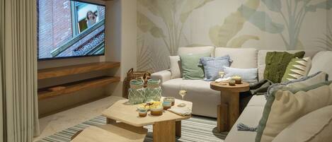 Uma sala de estar moderna com uma TV de tela plana, um sofá com almofadas, uma mesa de centro com objetos decorativos e um tapete estampado.