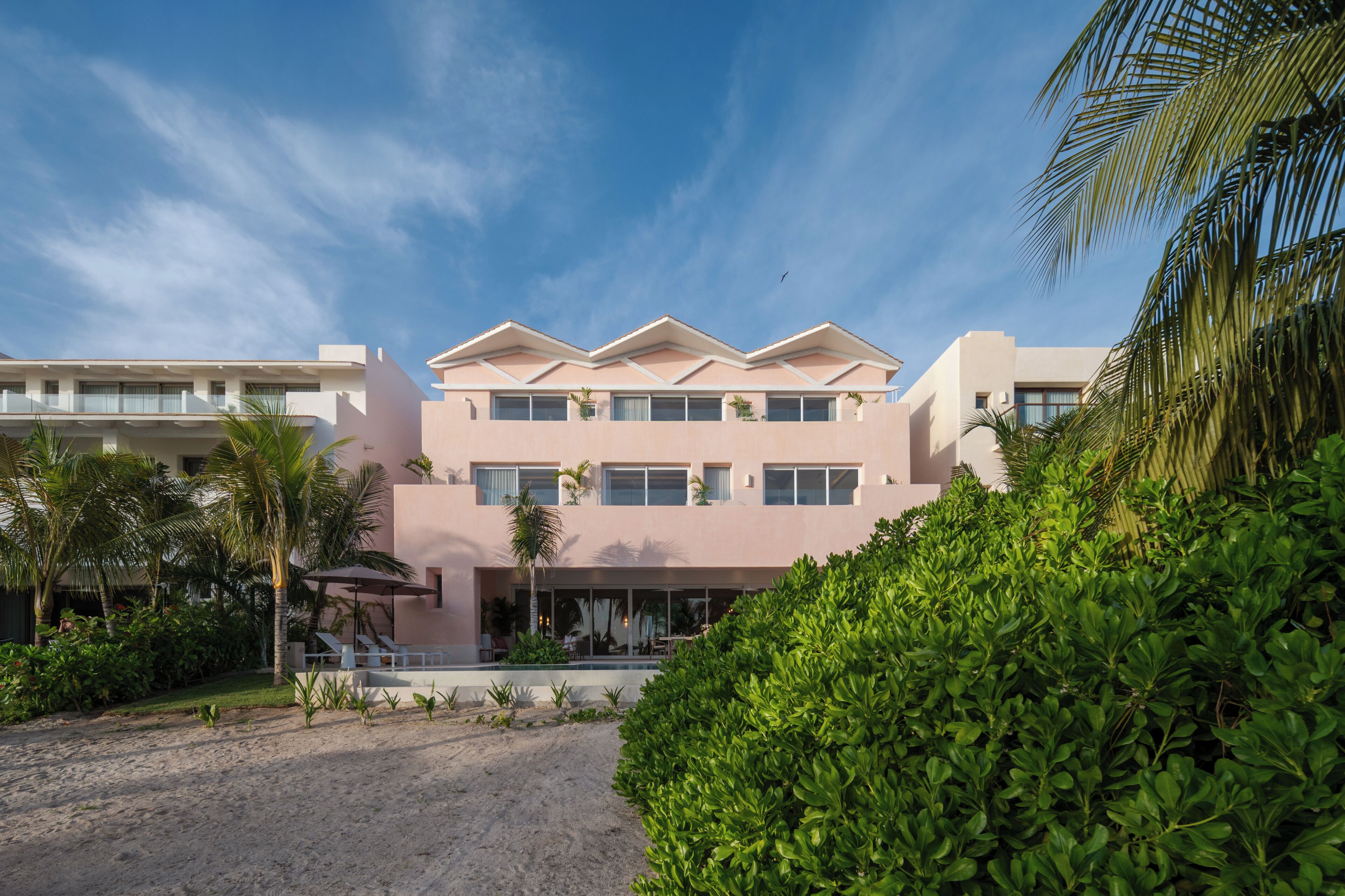 A modern hotel with a symmetrical facade, multiple balconies, and a pool area.