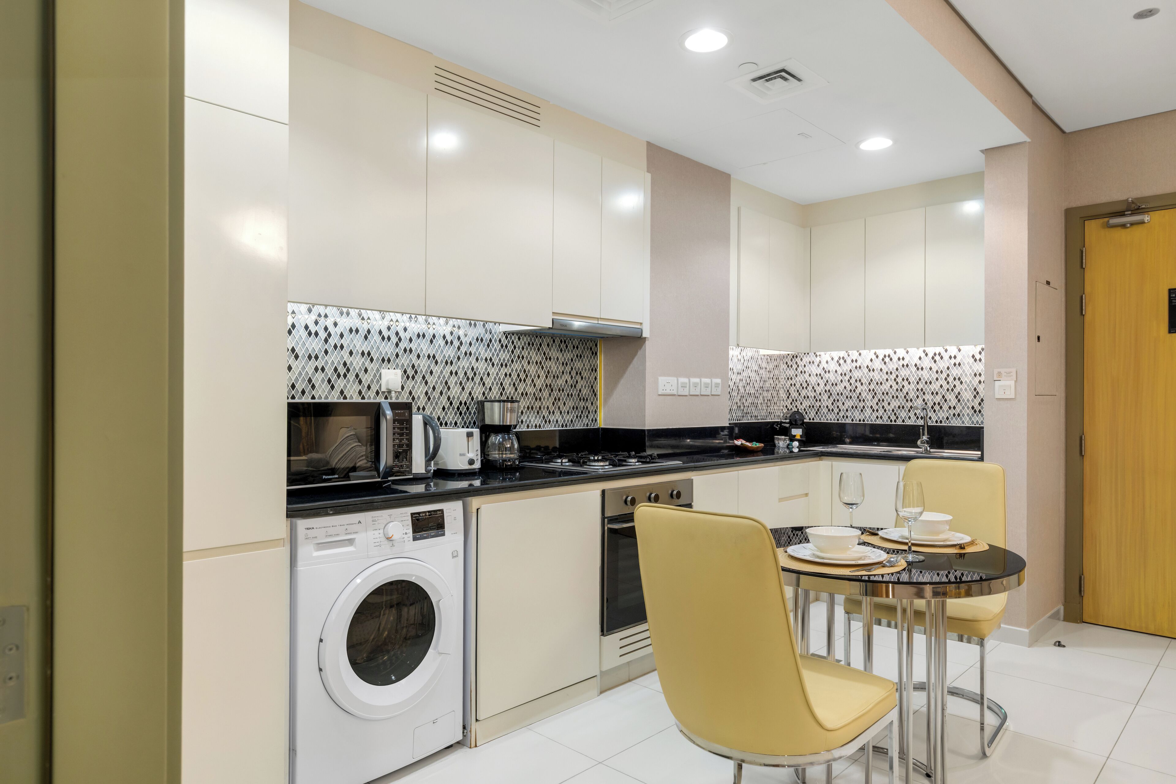 A compact kitchen with a washing machine, a dining table with chairs, and a wooden door.