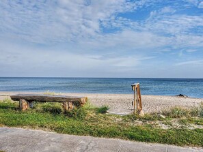 Une plage avec un banc en bois et une structure en bois, un ciel dégagé et l’océan en arrière-plan.