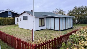 Moderni talo, jossa on suuri lasiseinäinen lisäosa, aidattu piha ja kirkas taivas.