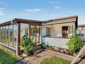 Une maison moderne dotée d’une véranda en verre, d’un petit jardin agrémenté de plantes en pot et d’une porte bien visible portant l’inscription « Uncen ».