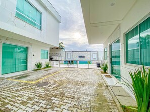 A modern building with a paved courtyard, large windows, and a pool area.