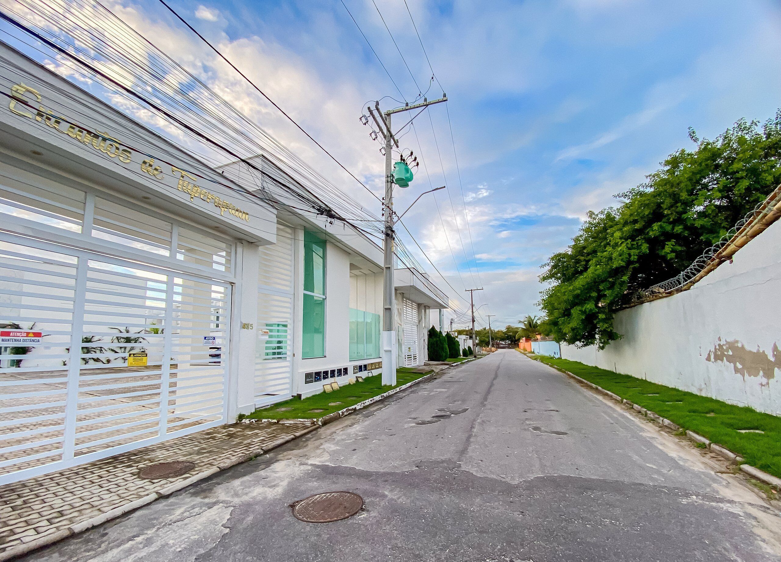 A street with a row of white buildings, some with signs indicating services like "ATM" and "ATMOSFERICA." There are power lines and a green traffic light visible.