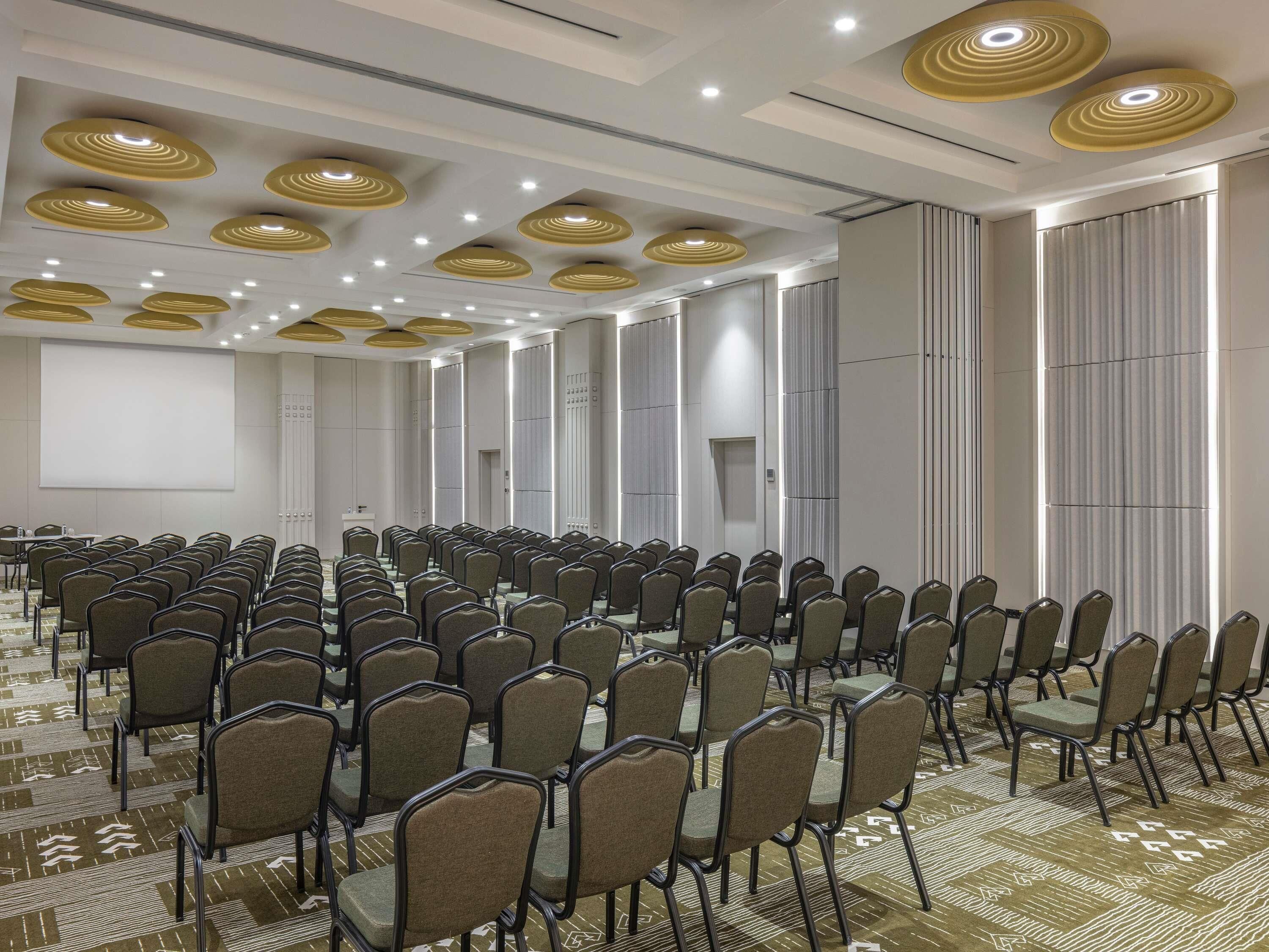 A conference room with rows of chairs, a projector screen, and recessed lighting.