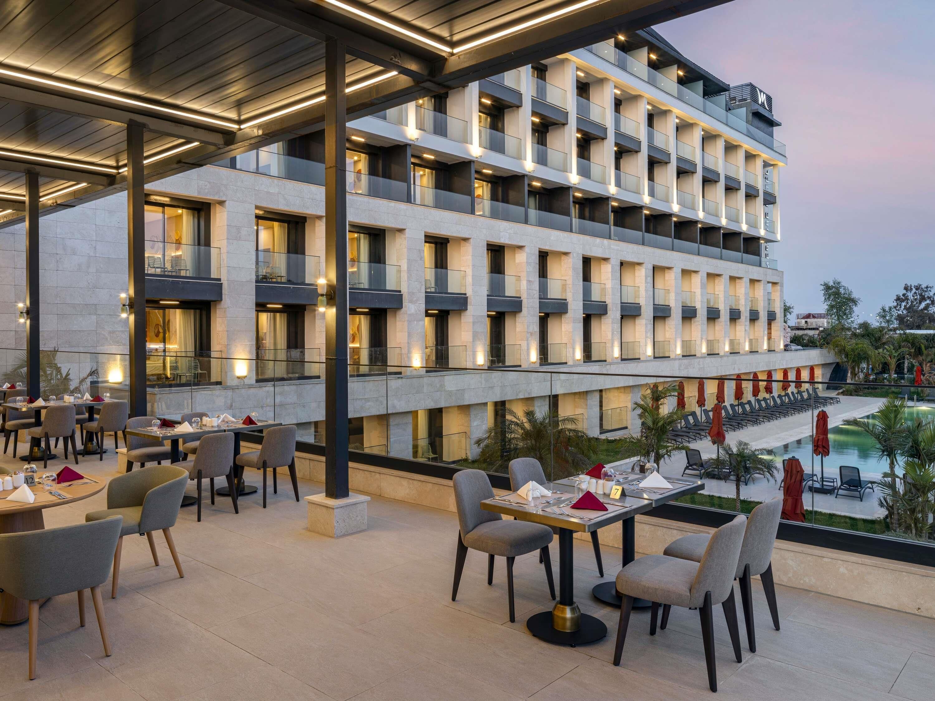 A hotel with outdoor dining areas, multiple floors, and a pool.