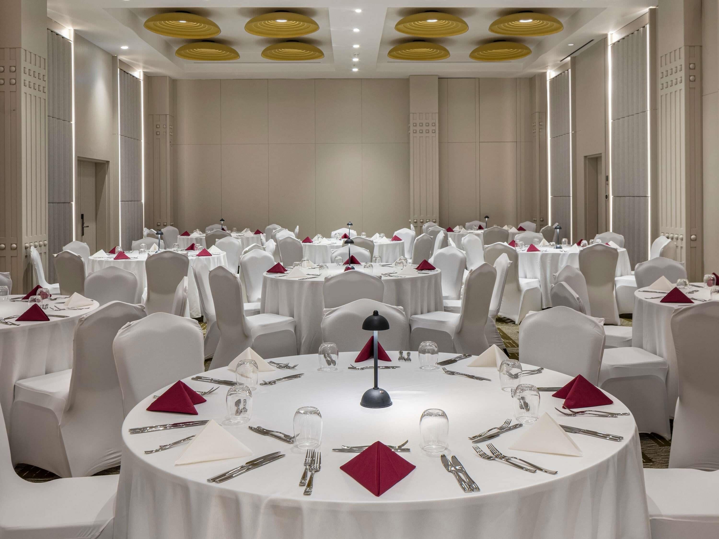 A banquet hall with round tables, white chairs, and red napkins.