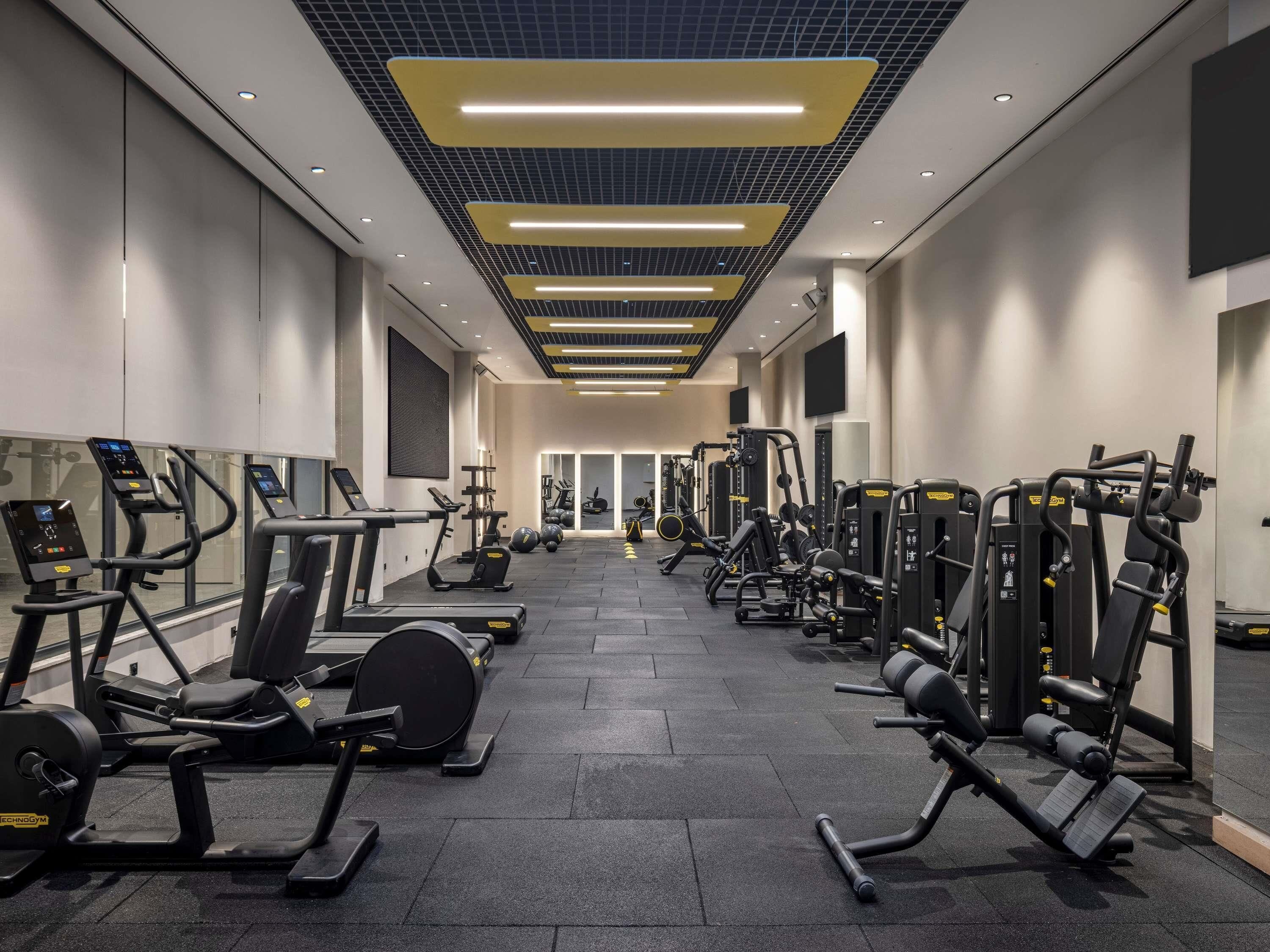 A gym with various exercise machines, a mirrored wall, and a modern ceiling design.