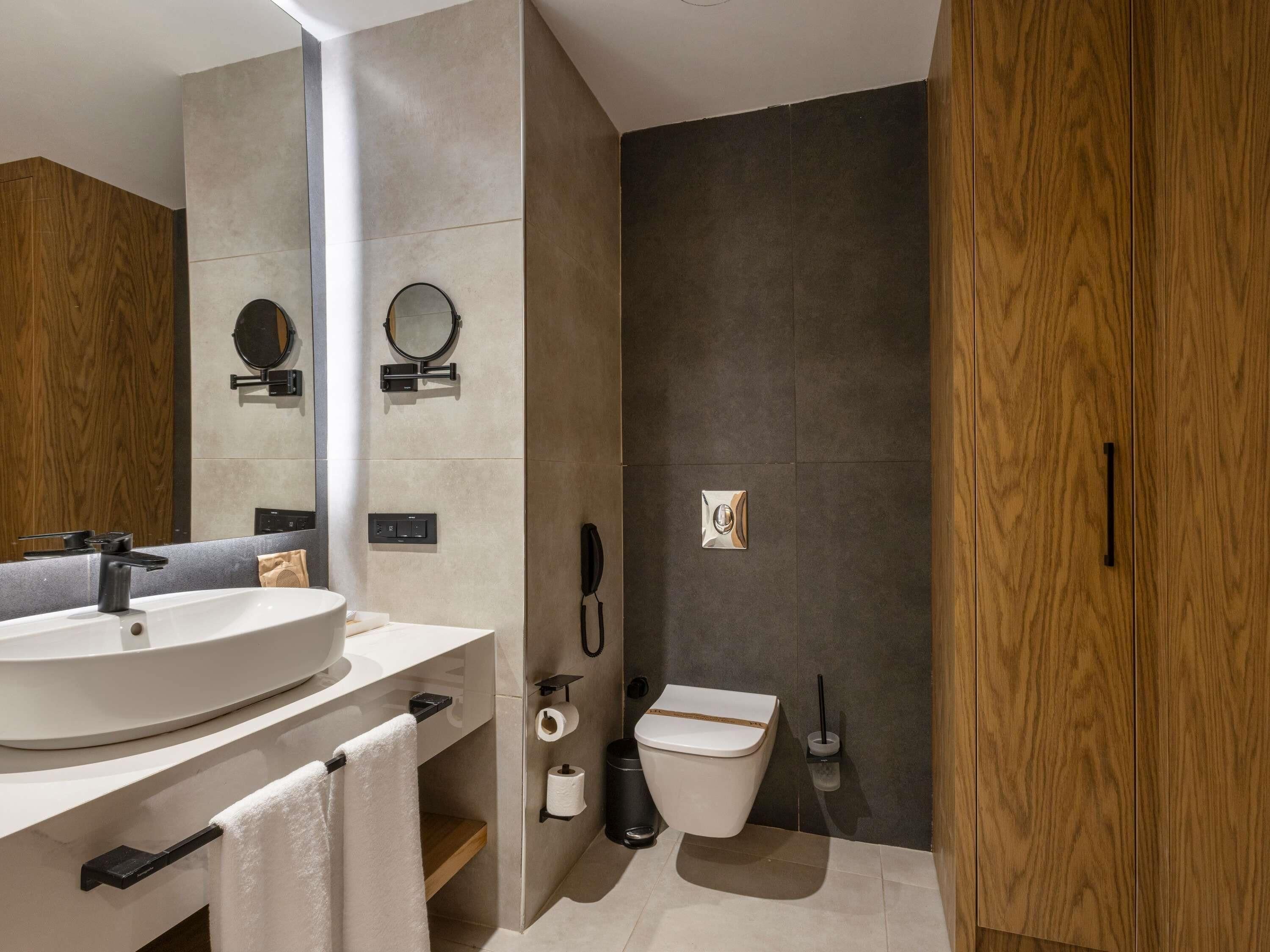 A modern bathroom with a large sink, mirror, toilet, and a wooden door.