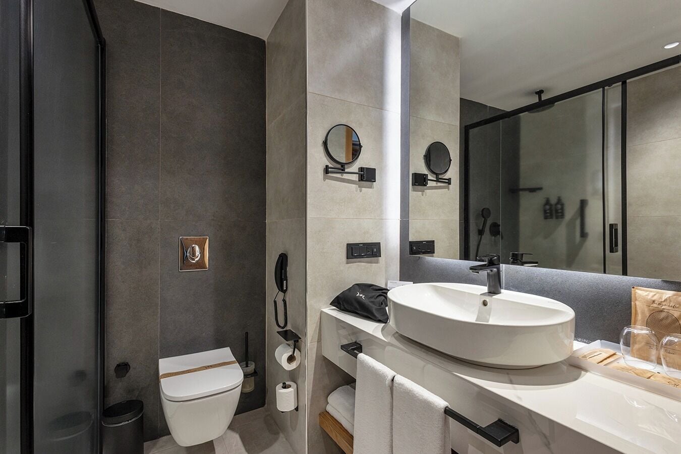 A modern bathroom with a white sink, a toilet, a mirror, and a shower area.