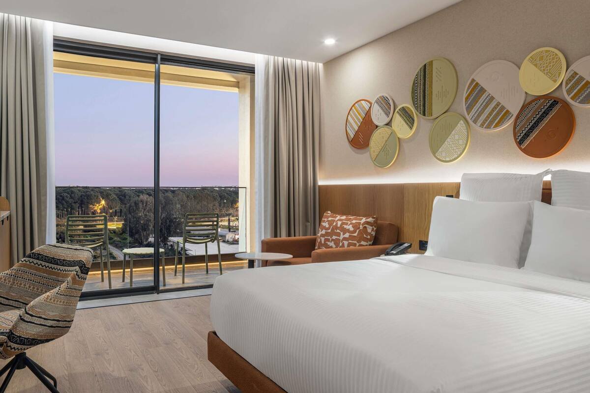A modern hotel room with a large bed, a balcony with a view, and decorative wall art.