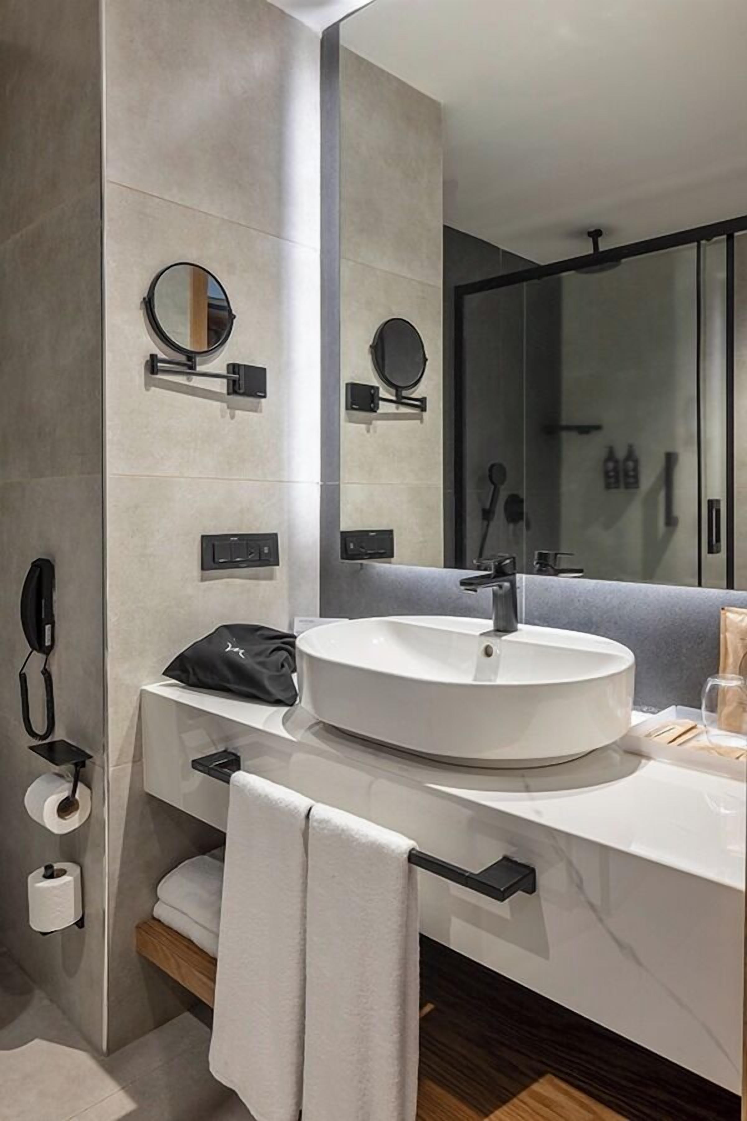Uma casa de banho moderna com uma sanita redonda, um espelho, um chuveiro e um porta-toalhas.