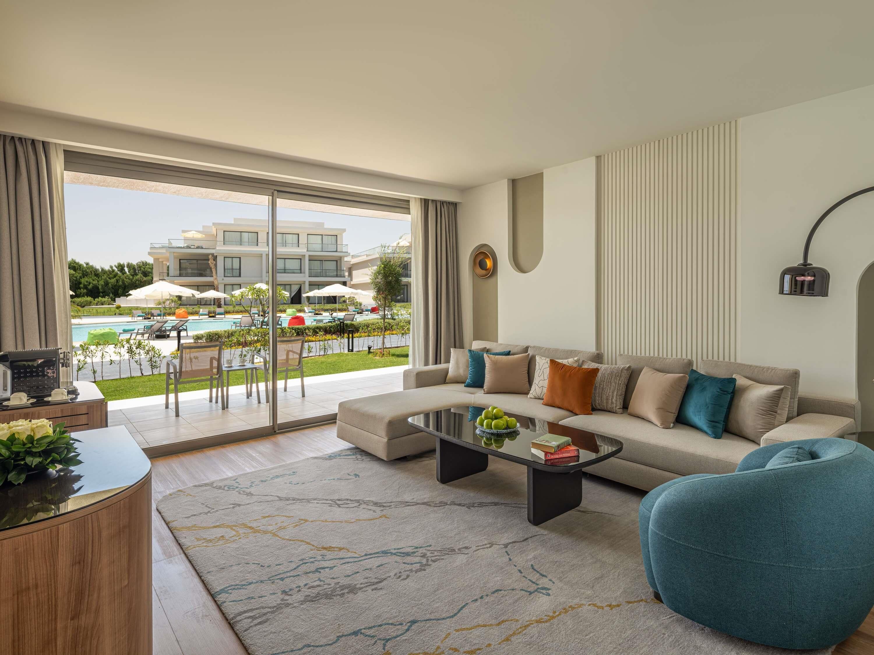 A modern living room with a sofa, coffee table, and a view of a pool and building.