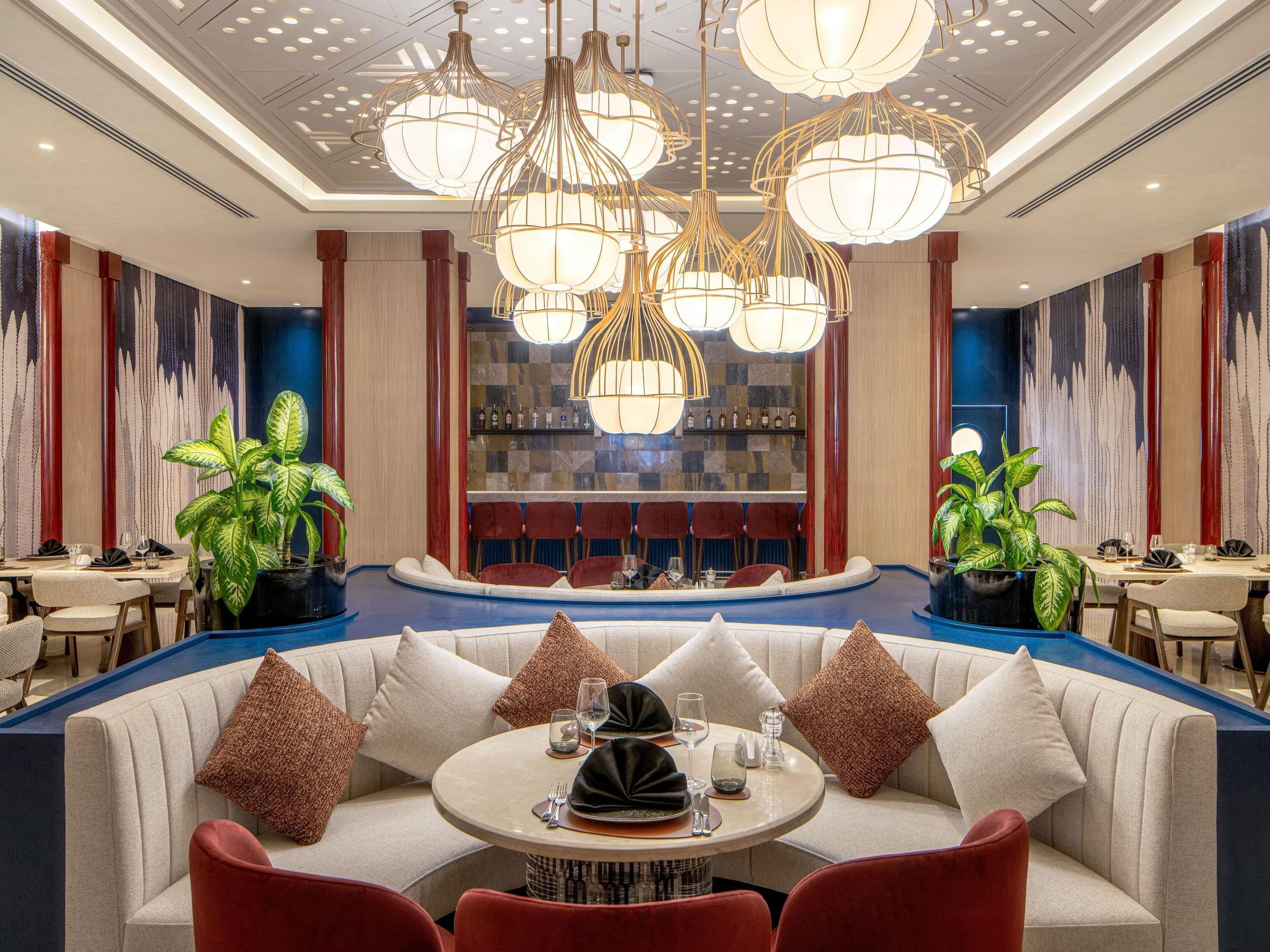 A modern interior with a round bar area, seating with red chairs, and a ceiling with unique lighting fixtures.