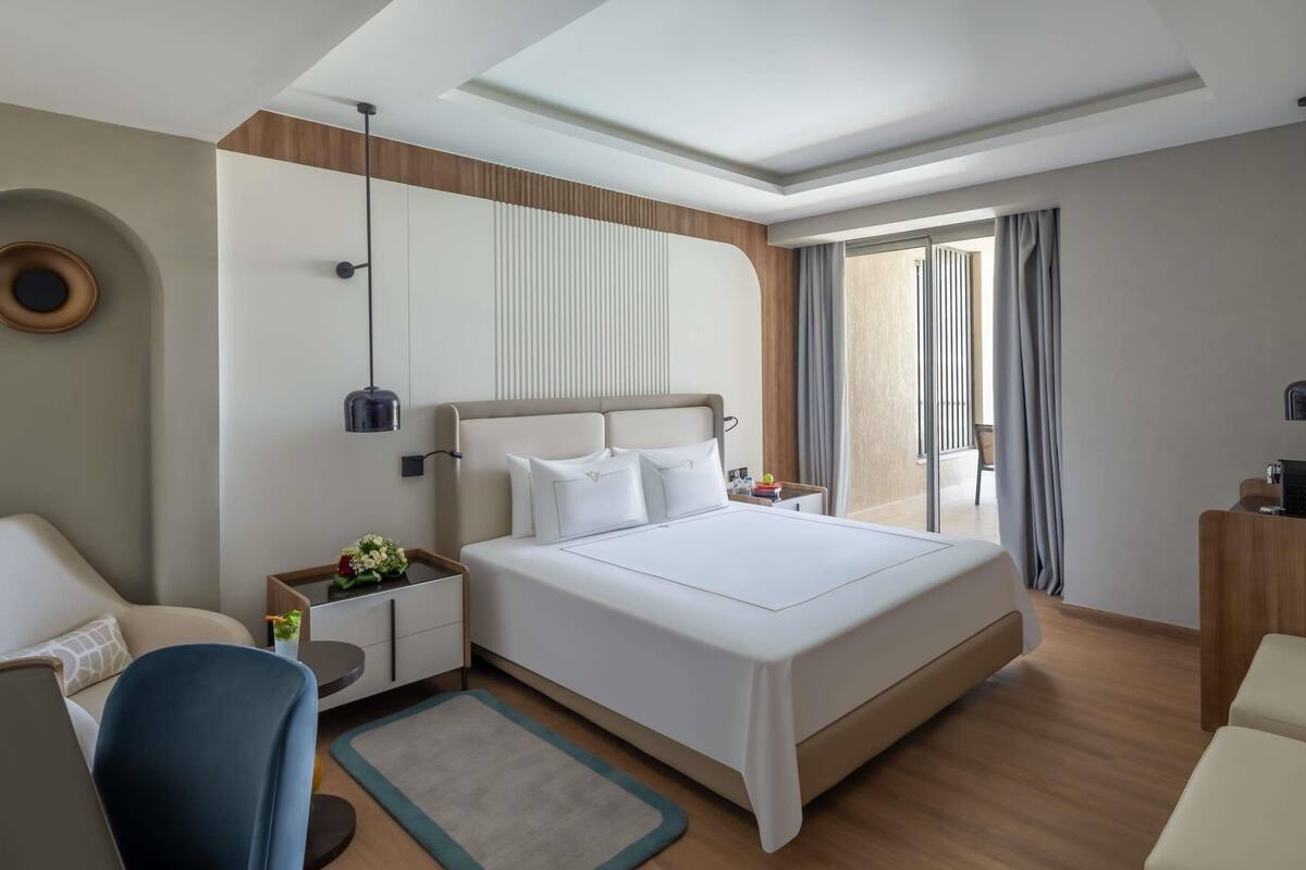 Une chambre d’hôtel moderne, dotée d’un grand lit, d’un bureau, d’une chaise et offrant une vue sur l’extérieur.