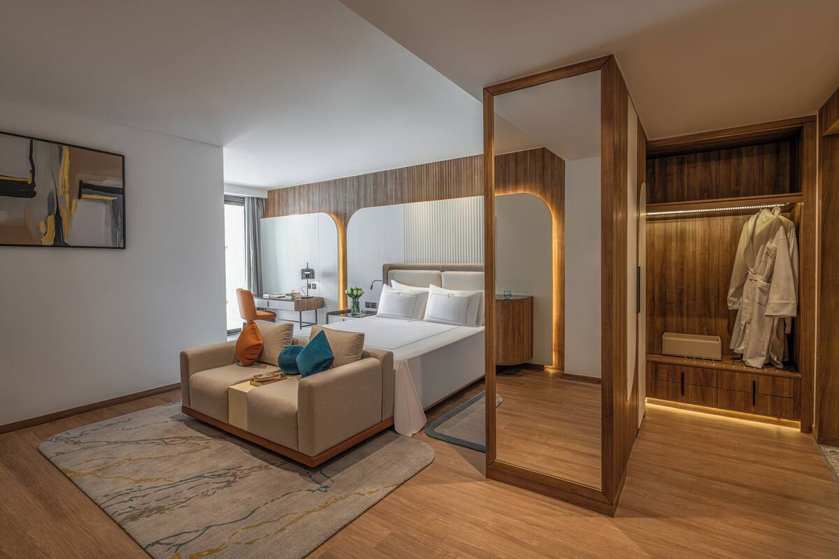 Une chambre d’hôtel moderne comprenant un lit, un coin salon, une coiffeuse et un dressing.