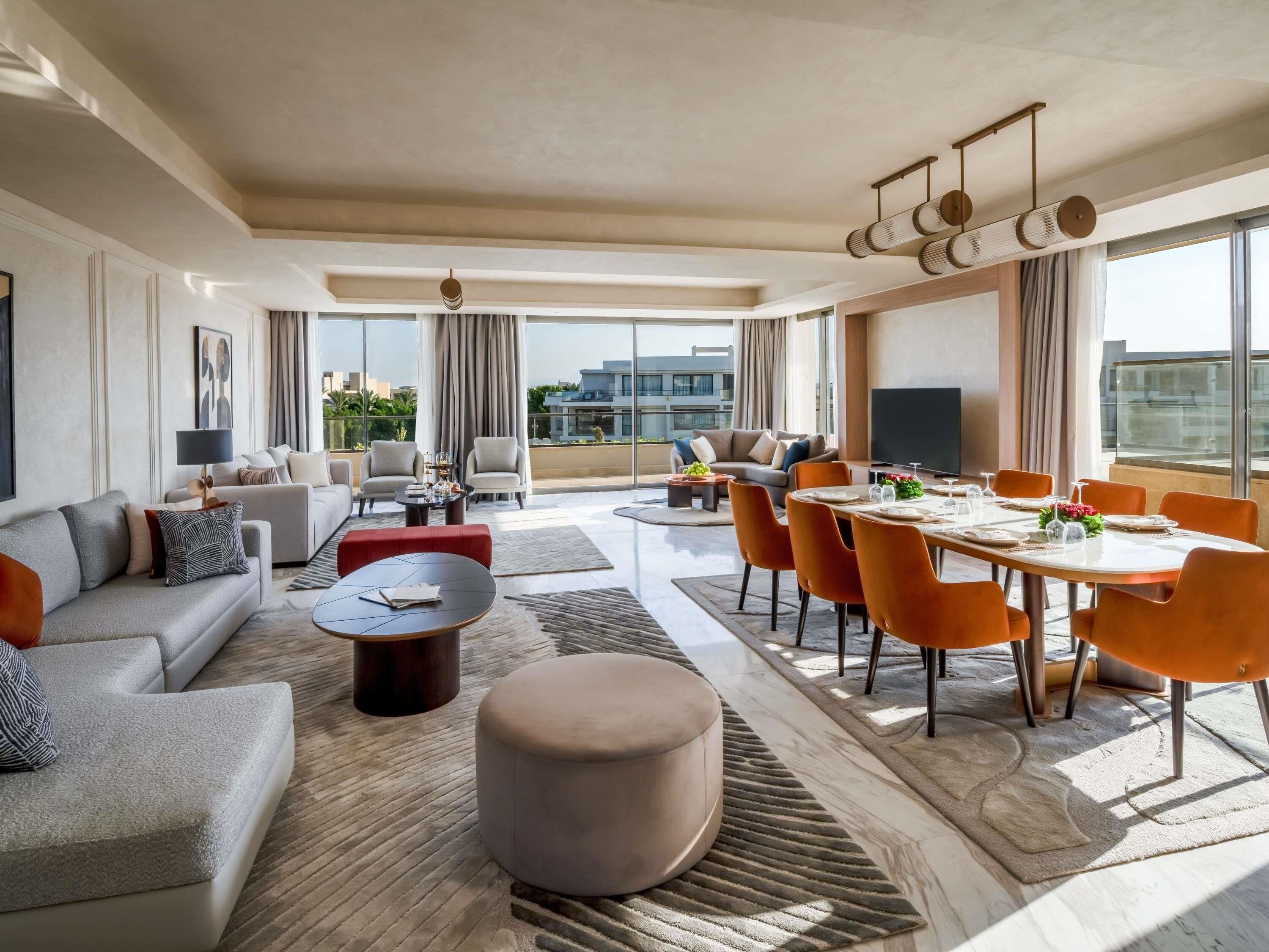 A modern living room with a sofa, ottoman, coffee table, and dining area with chairs and a table set for a meal.