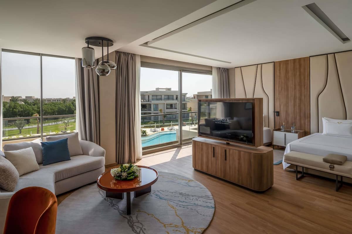 Une chambre d’hôtel moderne dotée d’une grande télévision, d’un canapé, d’un lit et offrant une vue sur une piscine.