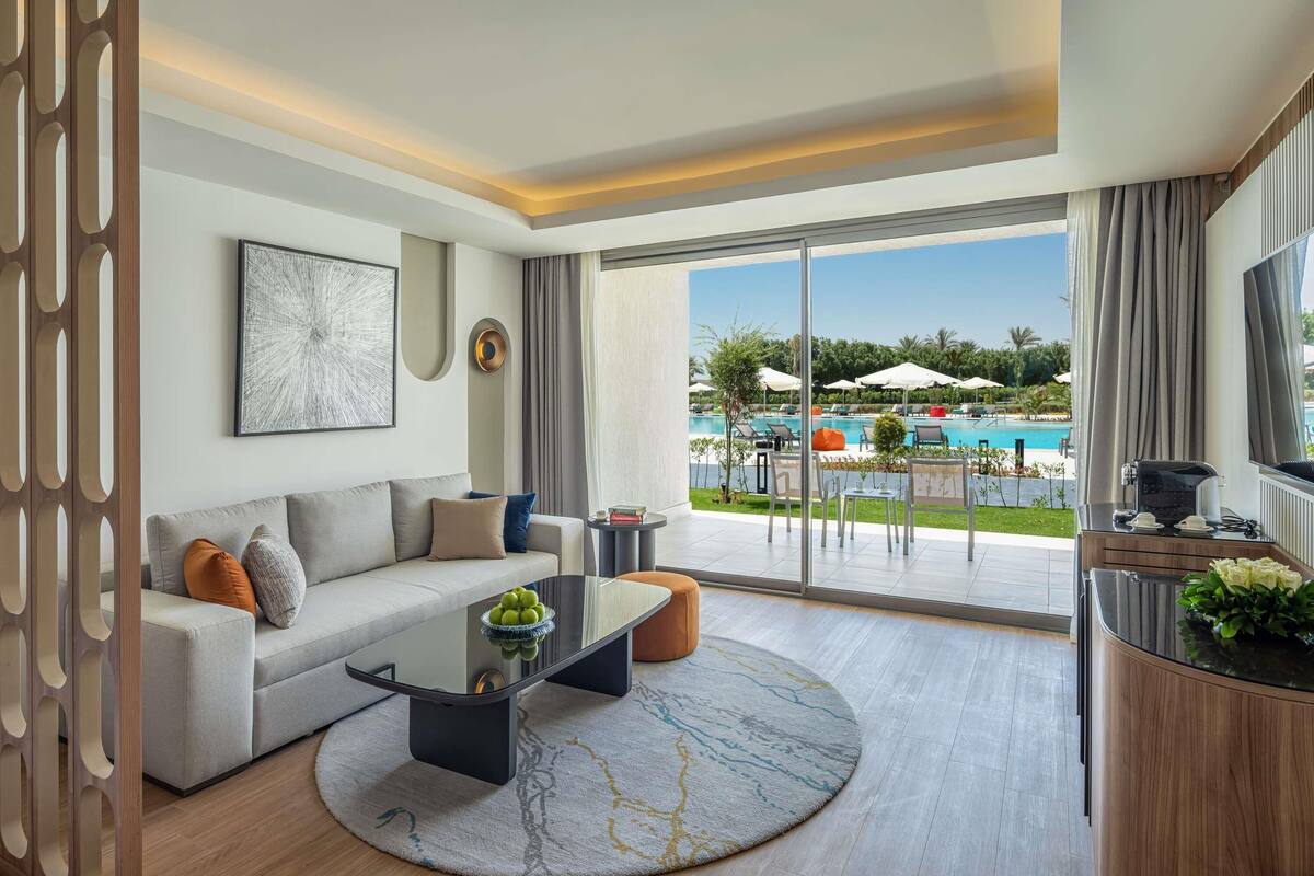 A modern living room with a sofa, coffee table, and a view of a pool.