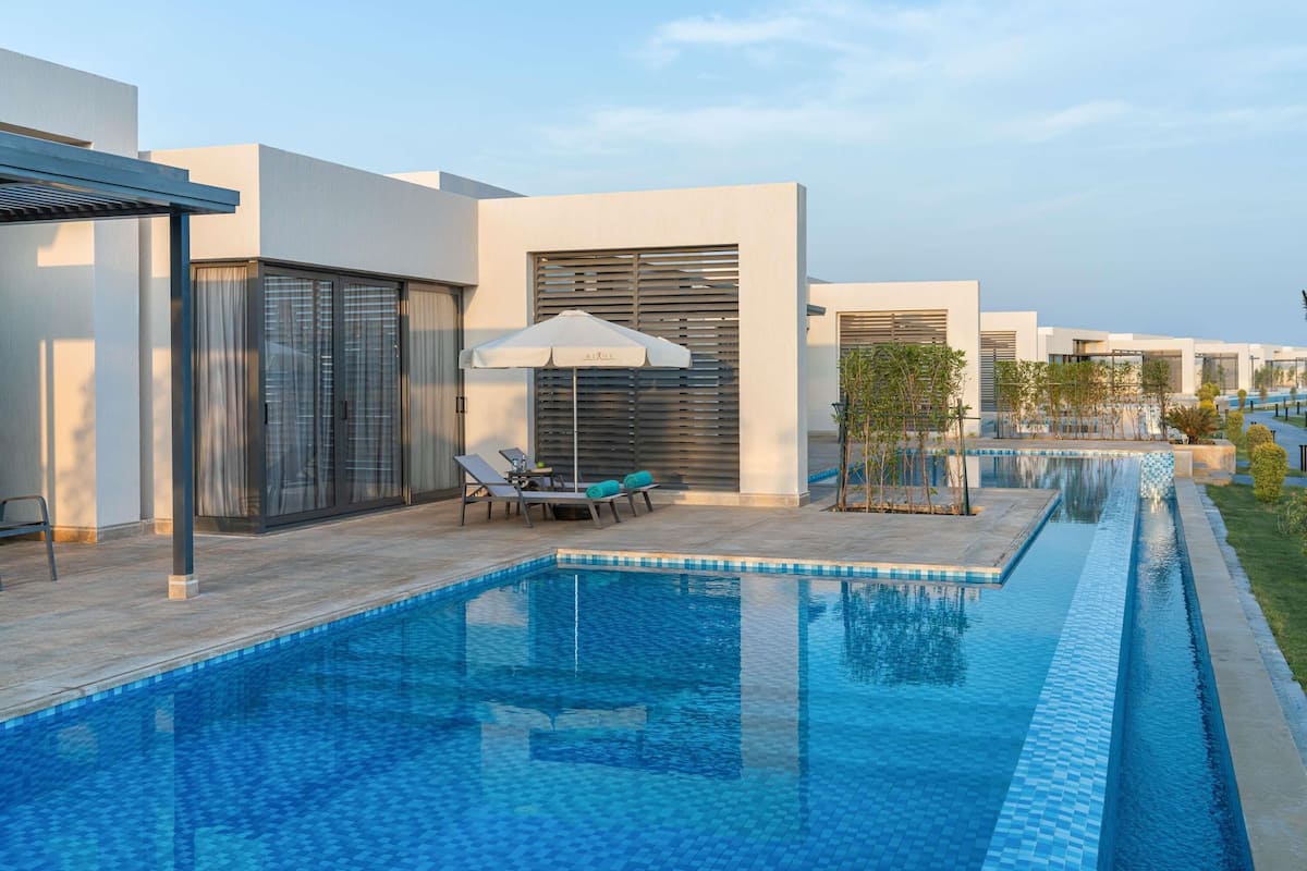 Un espace piscine extérieur moderne, doté de chaises longues et d’une pergola.