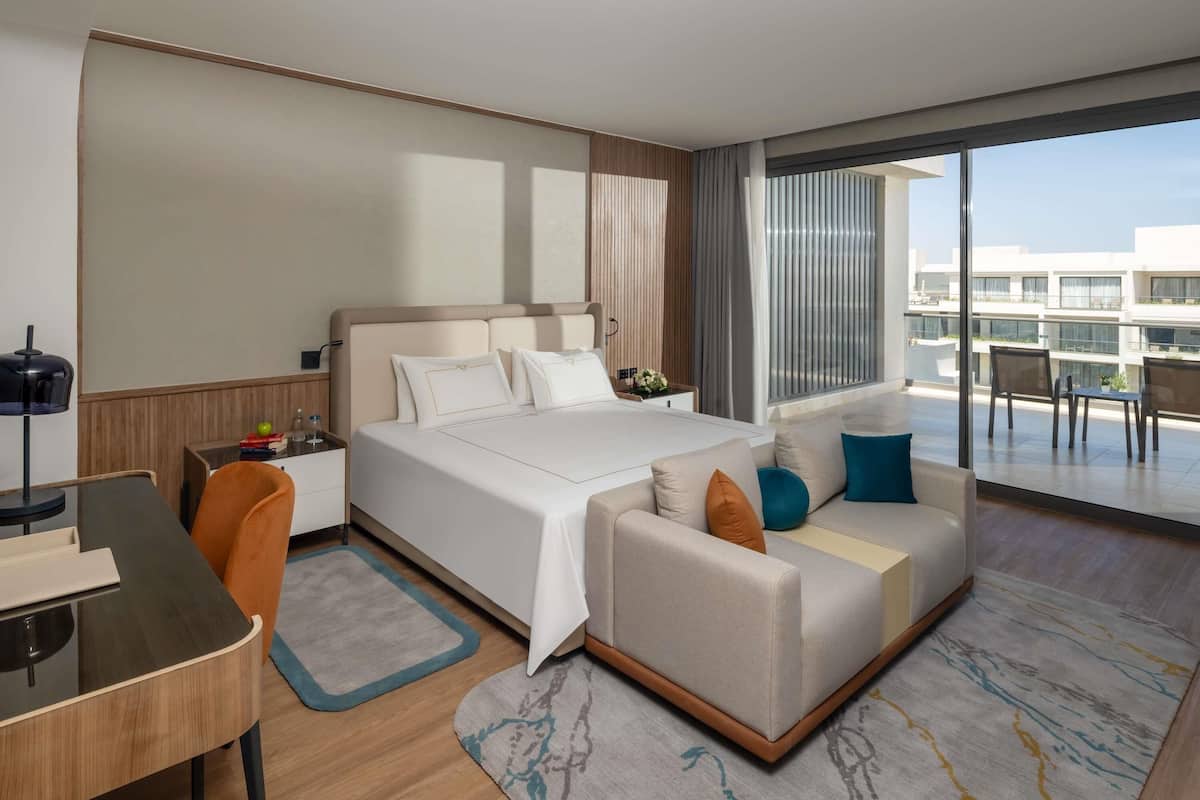 Une chambre d’hôtel moderne dotée d’un grand lit, d’un canapé, d’un bureau et d’un balcon offrant une vue sur les bâtiments.