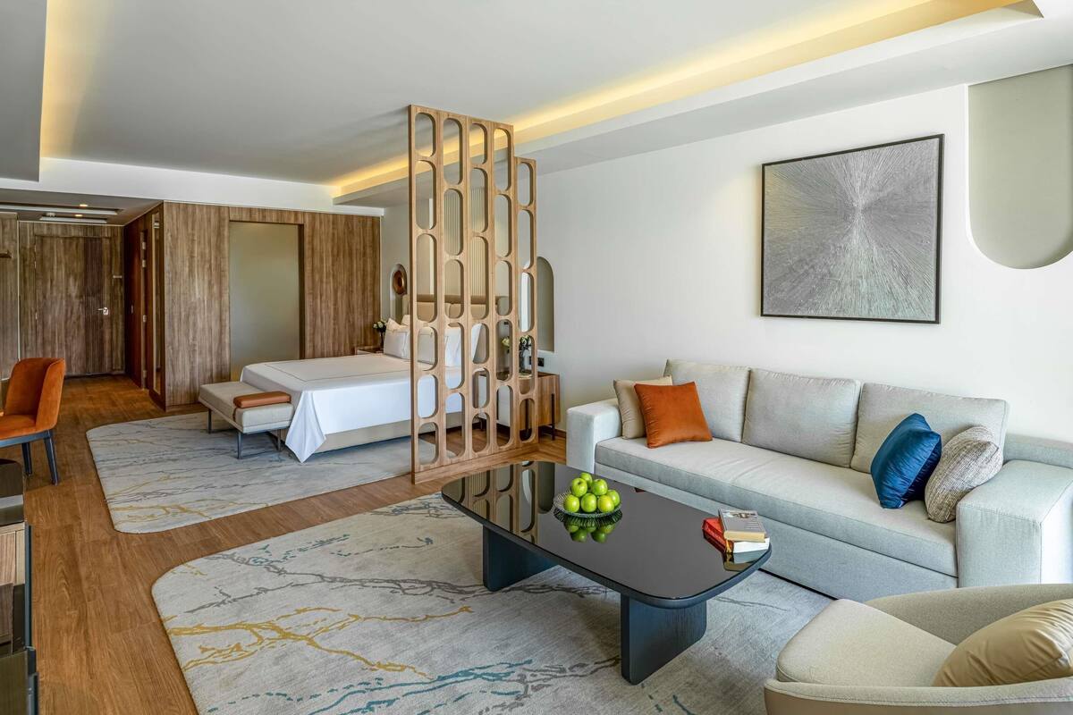 Une chambre d’hôtel moderne comprenant un lit, un canapé, une table basse et un élément de séparation décoratif.
