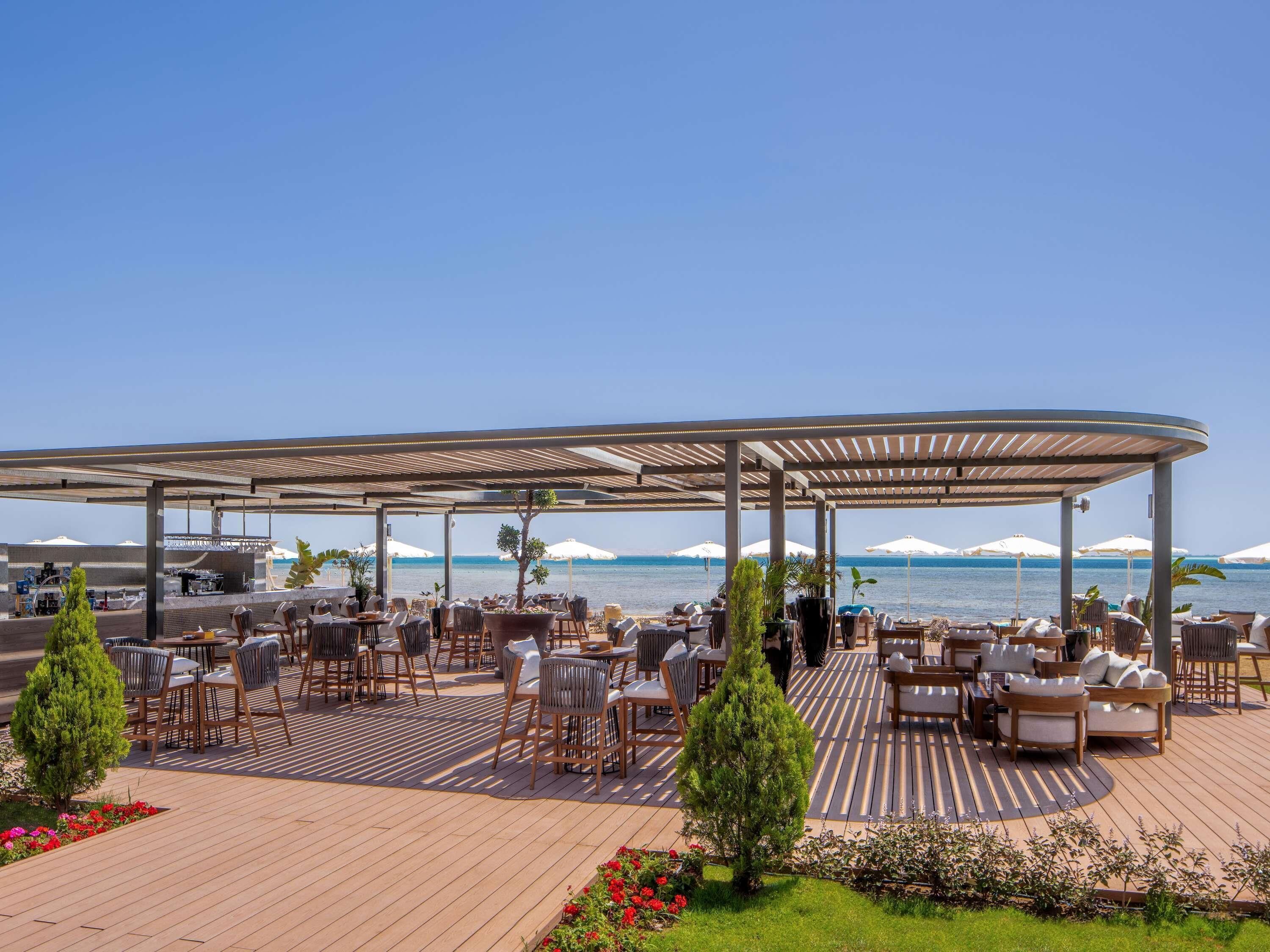 An outdoor seating area with tables and chairs, a covered section, and a view of the sea.
