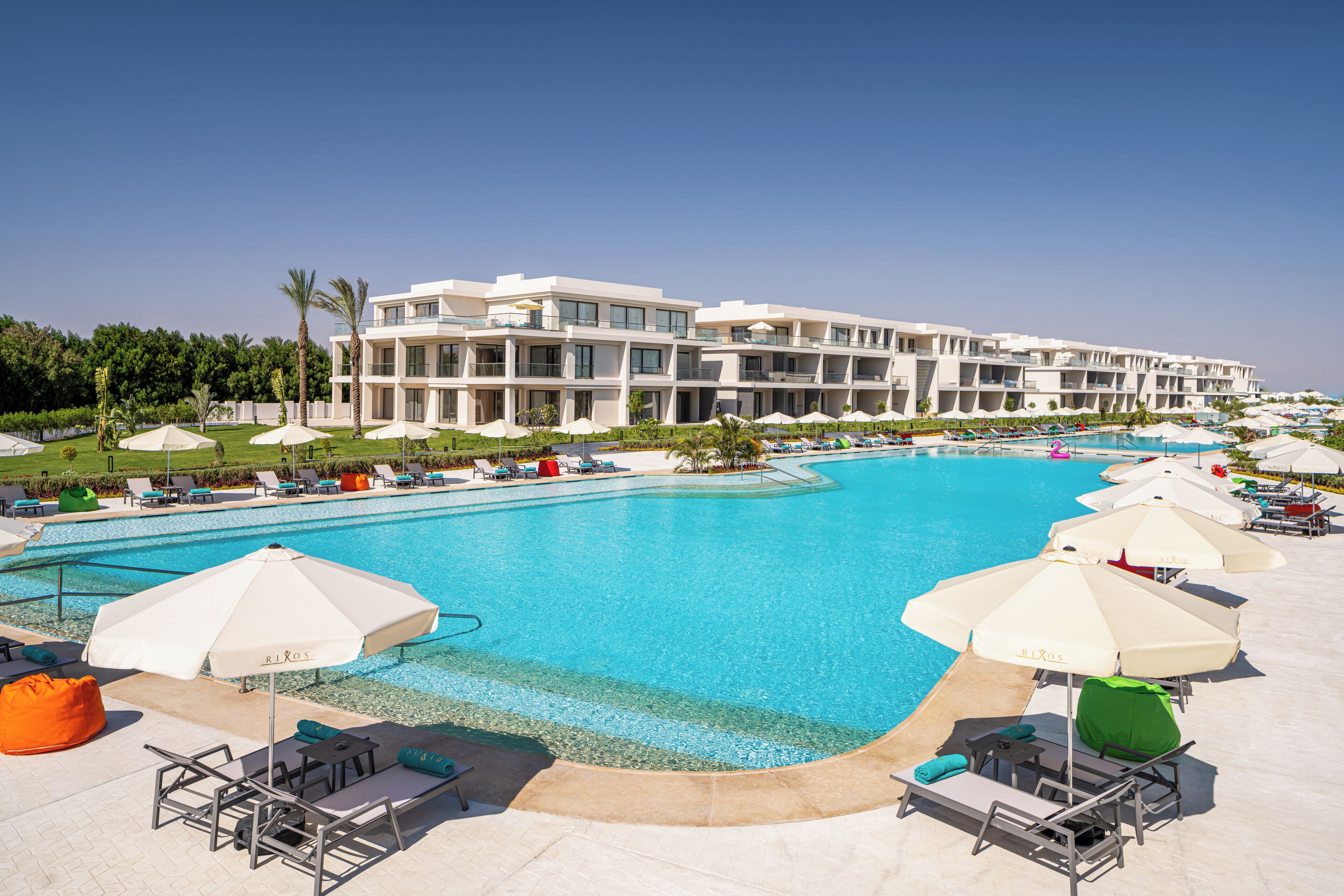 Un hôtel moderne doté d’une grande piscine, de chaises longues et de parasols.