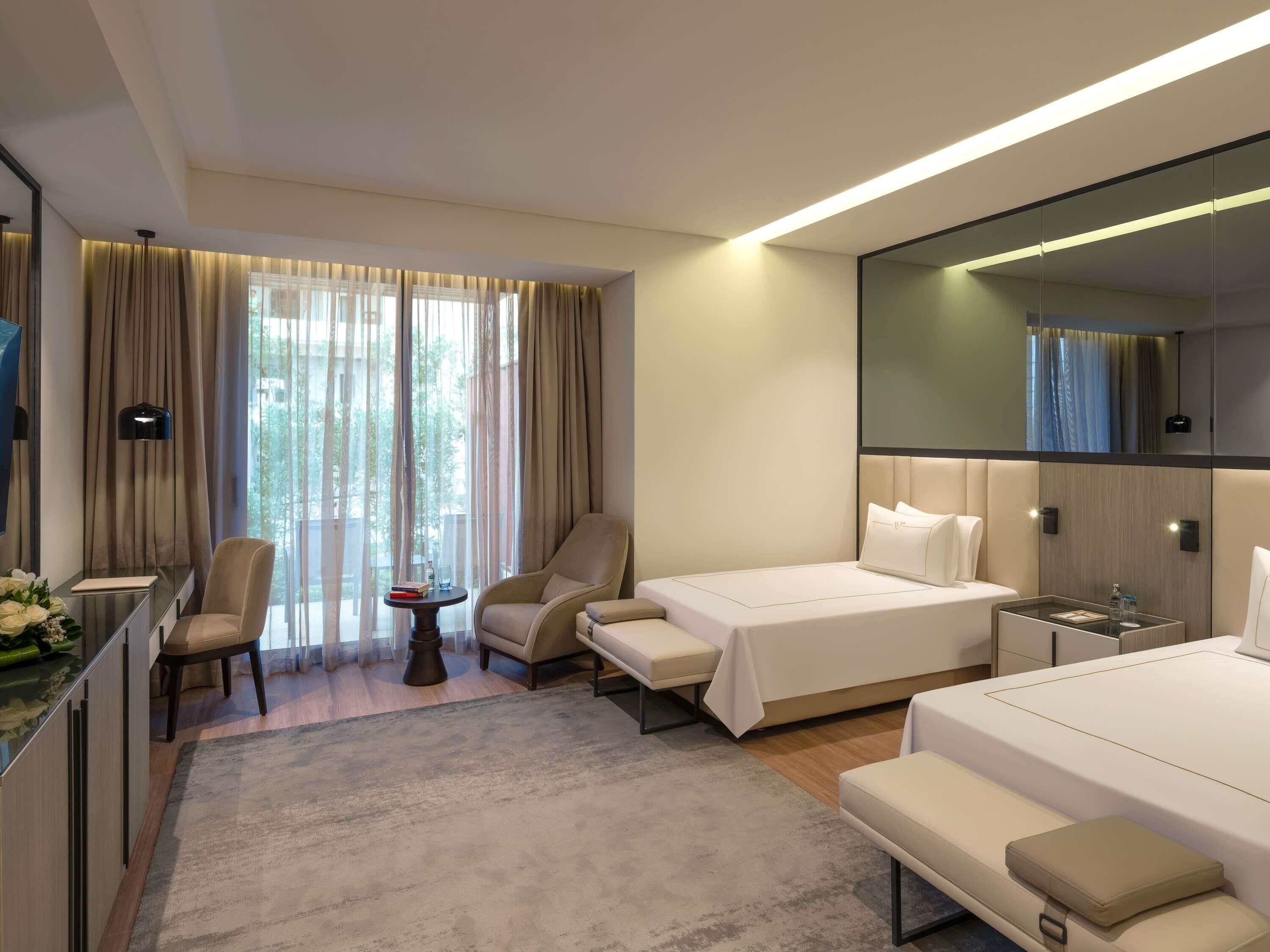 Ein Hotelzimmer mit Bett, Schreibtisch, Stuhl, kleinem Tisch und einem großen Spiegel.