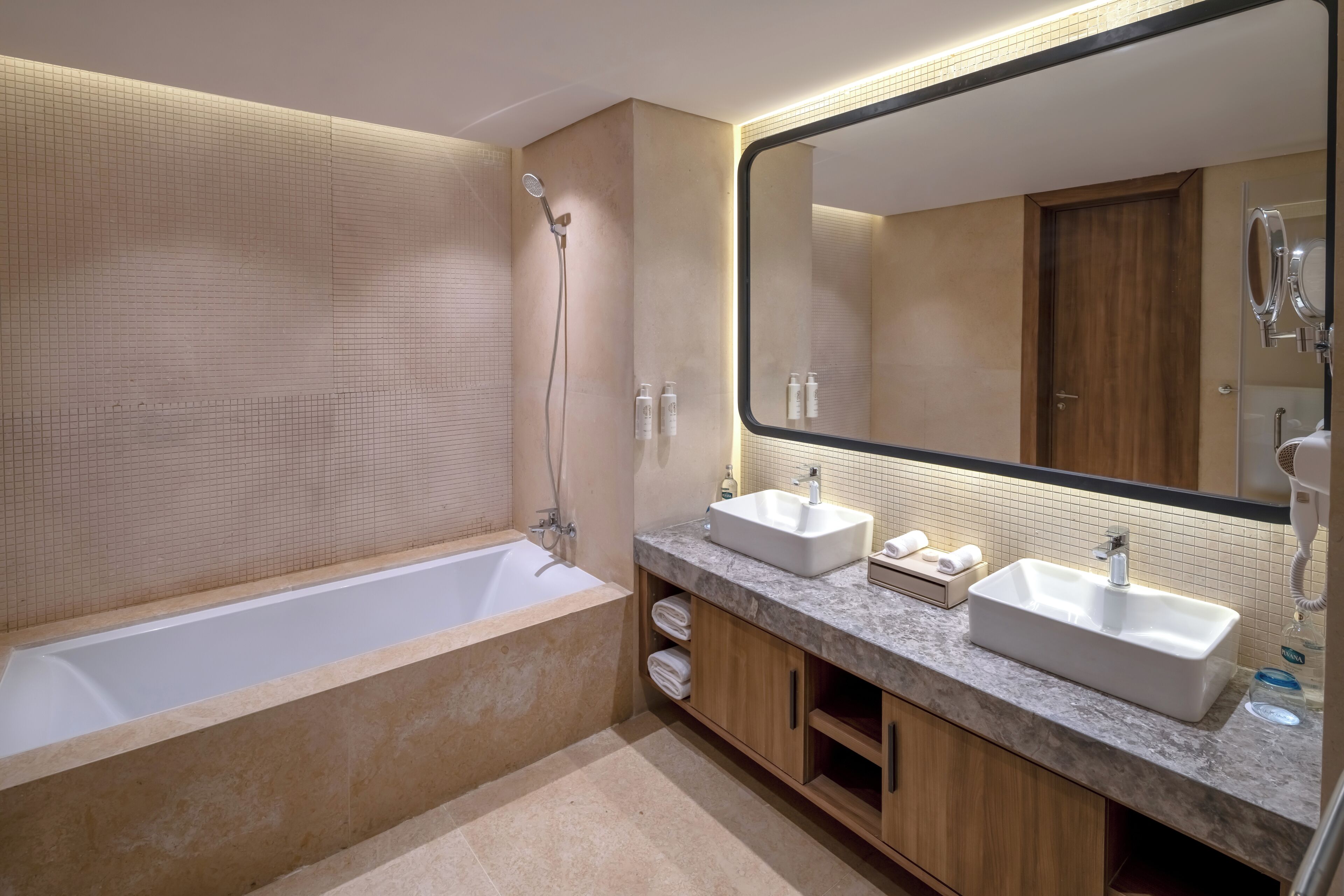 A modern bathroom with a bathtub, two sinks, a large mirror, and a shower.