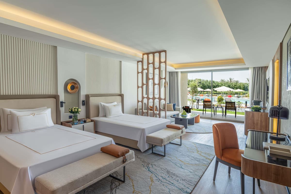 Une chambre d’hôtel avec deux lits, un bureau, une chaise et une vue sur l’espace extérieur de la piscine.