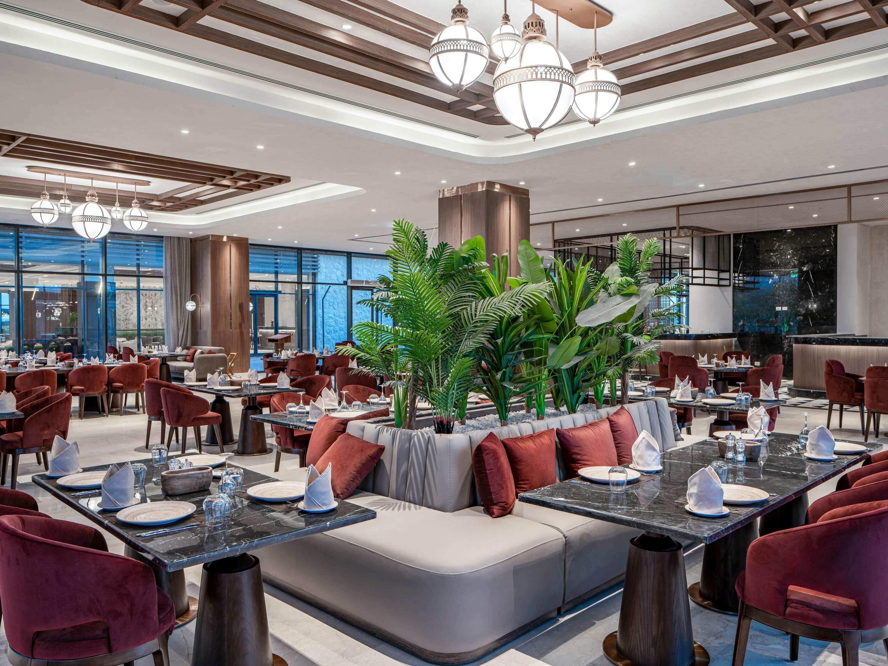 A modern dining area with round tables, red upholstered chairs, and a central seating area with a cushioned bench.