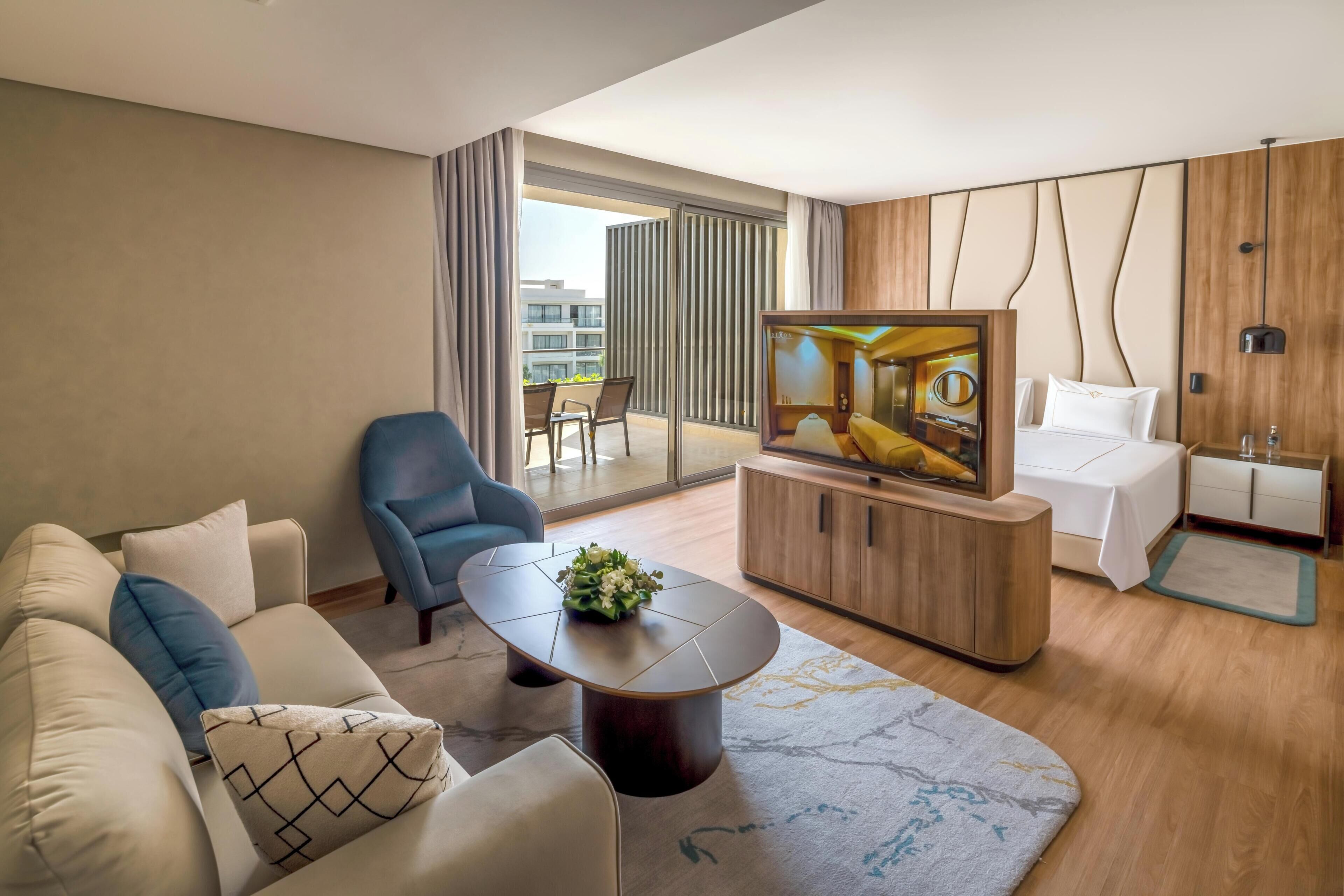 Habitación de hotel moderna con sofá, sillón, televisor y vistas al exterior.