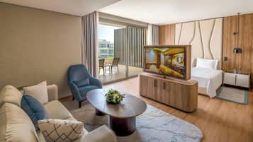 Habitación de hotel moderna con sofá, sillón, televisor y vistas al exterior.